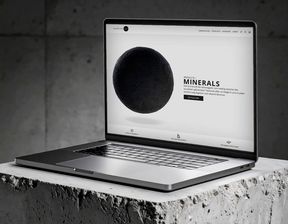 Laptop auf einem Betonblock zeigt die Startseite des Oberflächenwelt-Shops mit einer schwarzen Materialkugel